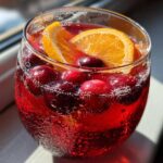 Close-up of a fizzy, red Thanksgiving punch garnished with fresh cranberries and an orange slice.