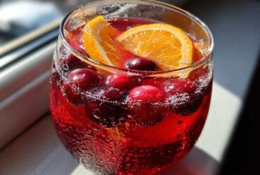 Close-up of a fizzy, red Thanksgiving punch garnished with fresh cranberries and an orange slice.