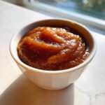 A close-up of thick, dark brown spiced pear butter served in a small white bowl.