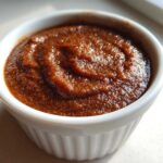 Close-up of thick, dark brown spiced pear butter swirled in a small white ramekin.