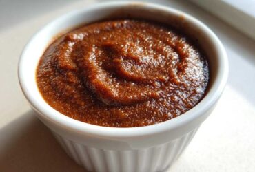 Close-up of thick, dark brown spiced pear butter swirled in a small white ramekin.