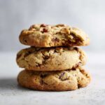 A stack of three golden brown butter pecan cookies, one on top is broken to show the chewy interior.