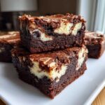 Two stacked, fudgy cream cheese brownies showing a rich dark chocolate base and a marbled cream cheese swirl.