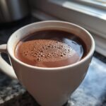 Close-up of a white mug filled with rich, dark french hot chocolate topped with small bubbles.