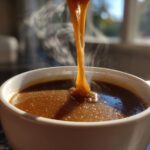 Close-up of thick, steaming homemade brown gravy being poured into a white bowl.