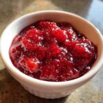 A close-up of bright red, chunky strawberry freezer jam served in a small white ramekin.