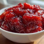 Close-up of vibrant, chunky strawberry freezer jam filling a small white bowl, glistening in the light.