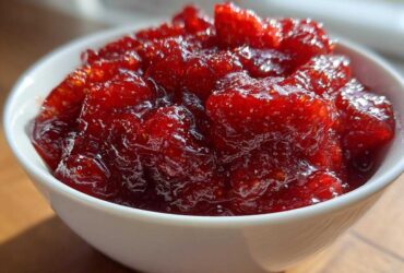 Close-up of vibrant, chunky strawberry freezer jam filling a small white bowl, glistening in the light.