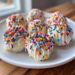 A plate of homemade sugar cookie truffles coated in white chocolate and covered in colorful rainbow sprinkles.