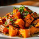 Close-up of roasted orange cubes in a vibrant sweet potato salad, garnished with dried cranberries and fresh parsley.