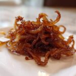 Close-up of a small pile of rich, dark brown caramelized onions on a white square plate.