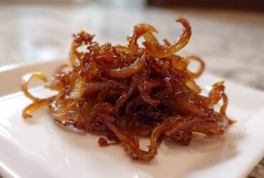 Close-up of a small pile of rich, dark brown caramelized onions on a white square plate.
