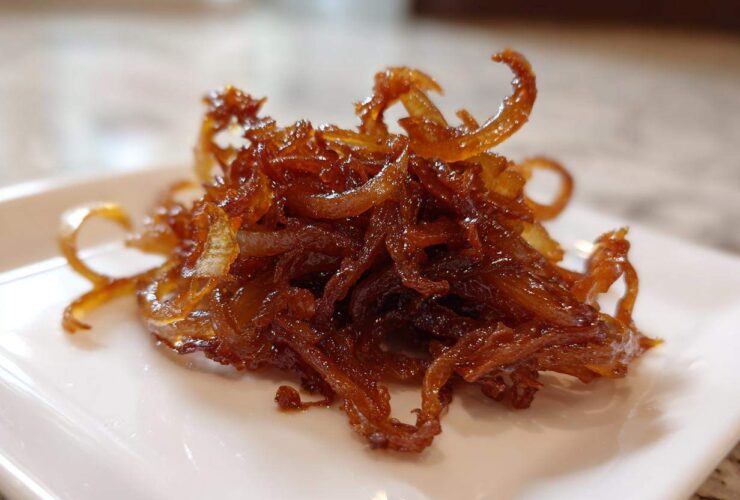 Close-up of a small pile of rich, dark brown caramelized onions on a white square plate.