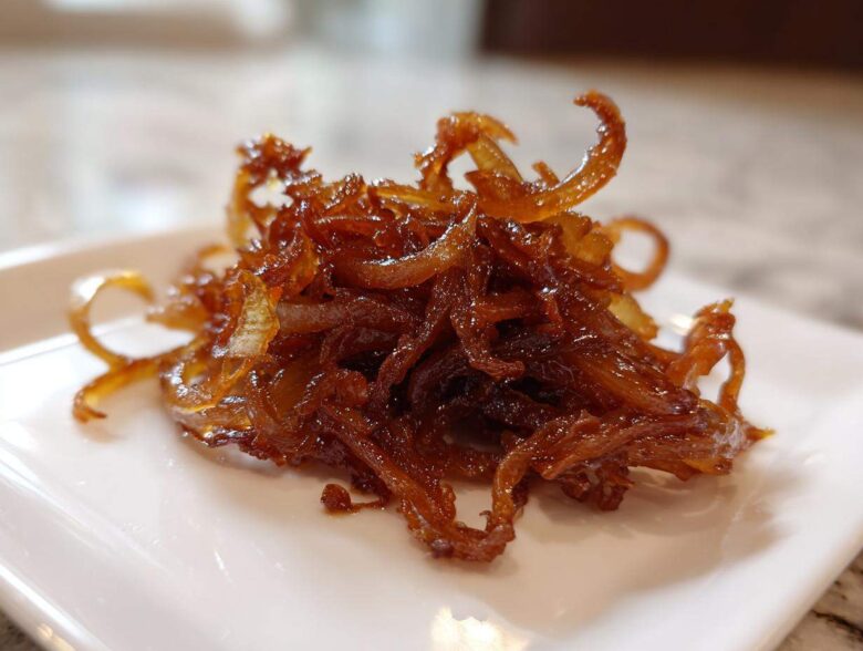 Close-up of a small pile of rich, dark brown caramelized onions on a white square plate.