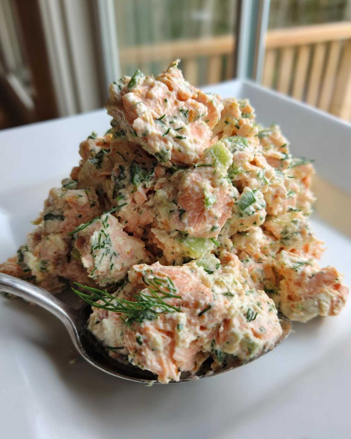 A spoonful of creamy, chunky salmon salad mixed with dill and celery, ready to eat.