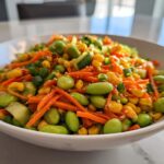 Close-up of a bright edamame salad featuring shelled edamame, shredded carrots, corn, and cucumber.