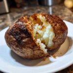 A close-up of a perfectly cooked air fryer baked potato, split open to reveal fluffy white interior and seasoned, crispy skin.