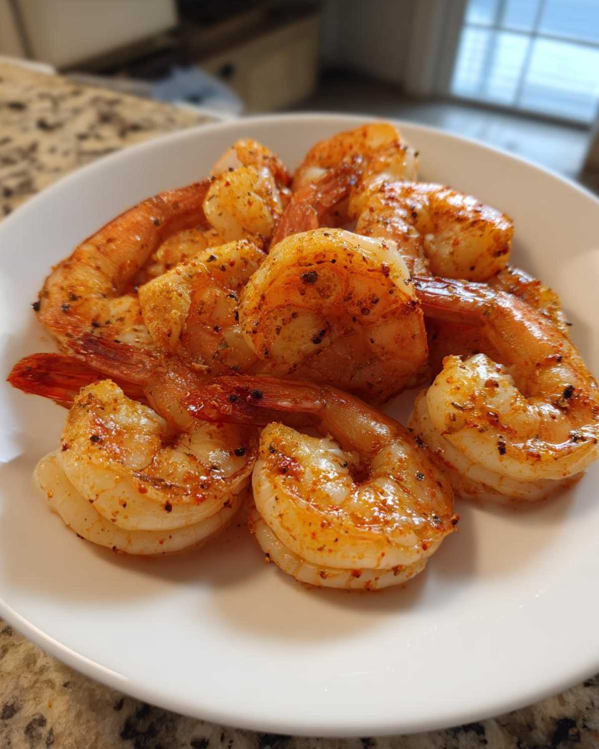 Close-up of seasoned, cooked air fryer frozen shrimp piled on a white plate.
