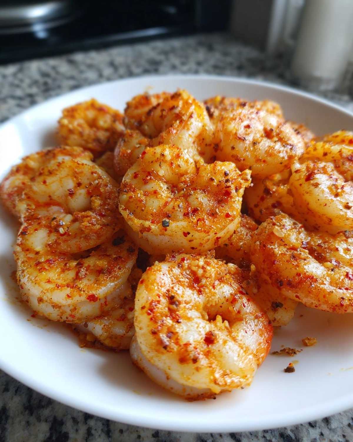 Close-up of perfectly cooked air fryer frozen shrimp seasoned with red spices on a white plate.