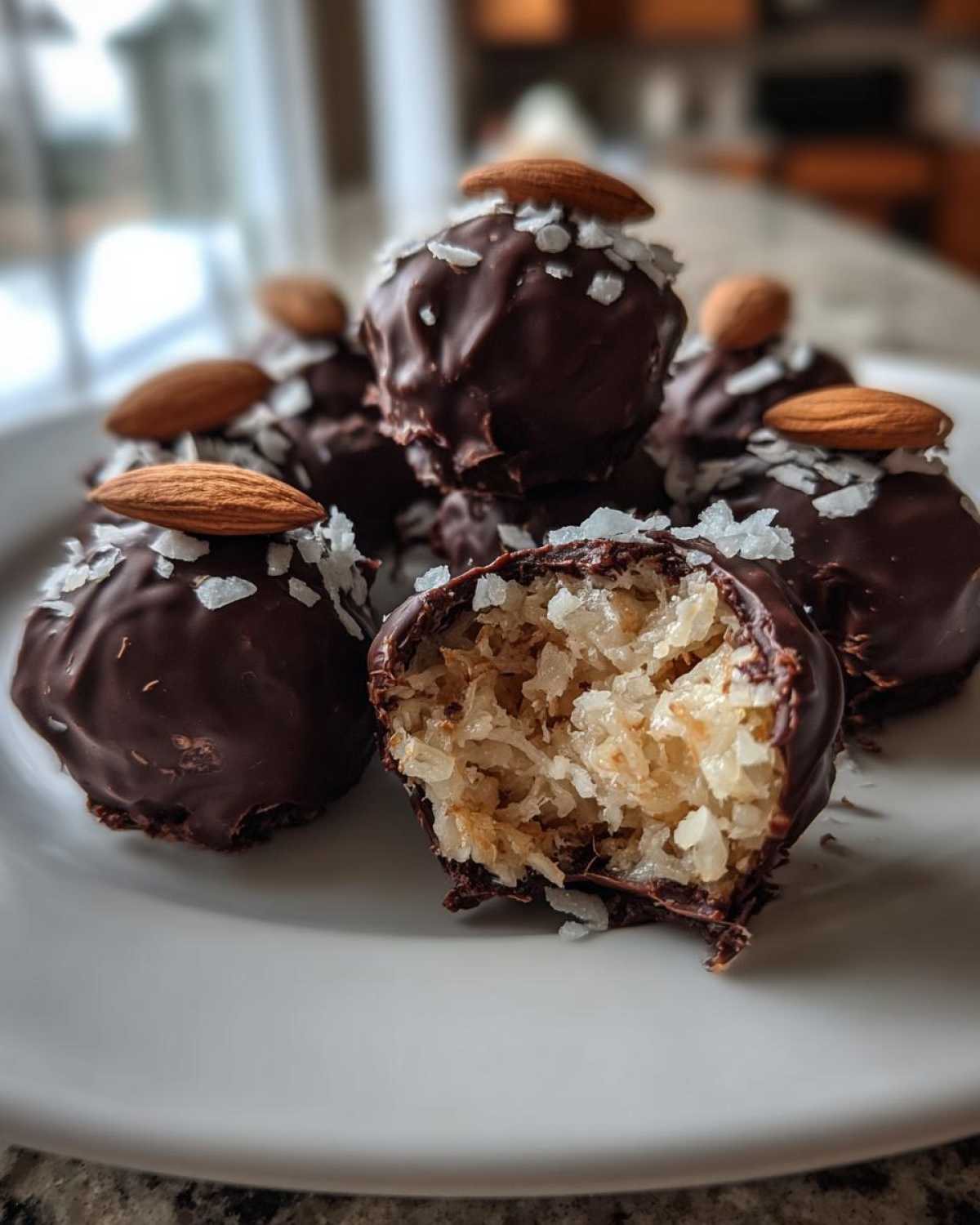 A plate of homemade almond joy truffles, one cut open revealing the shredded coconut center, topped with coconut flakes and a whole almond.