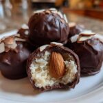 A pile of homemade almond joy truffles, one cut open revealing coconut filling and a whole almond inside.