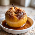 Close-up of a single, golden baked apples dessert sitting in a pool of caramel sauce.