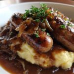 Close-up of delicious bangers and mash topped with caramelized onions and rich brown gravy.