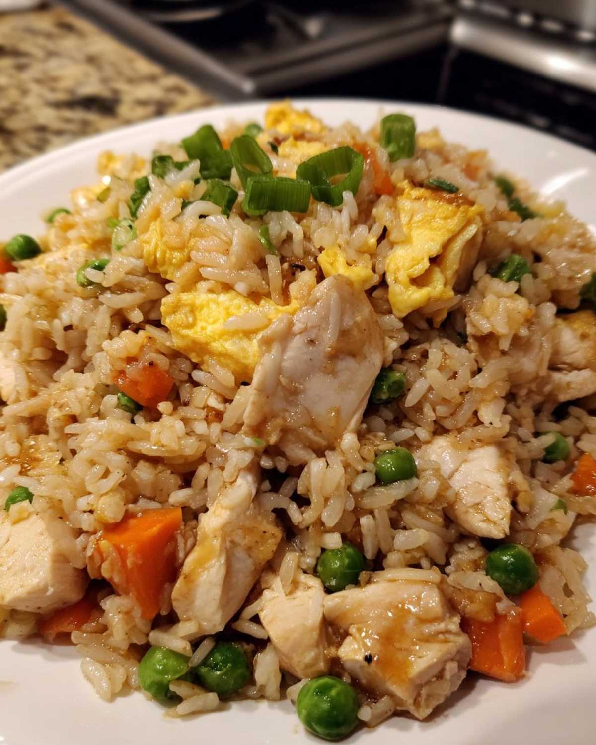 A close-up serving of delicious chicken fried rice featuring white chicken pieces, scrambled egg, peas, carrots, and green onion garnish.