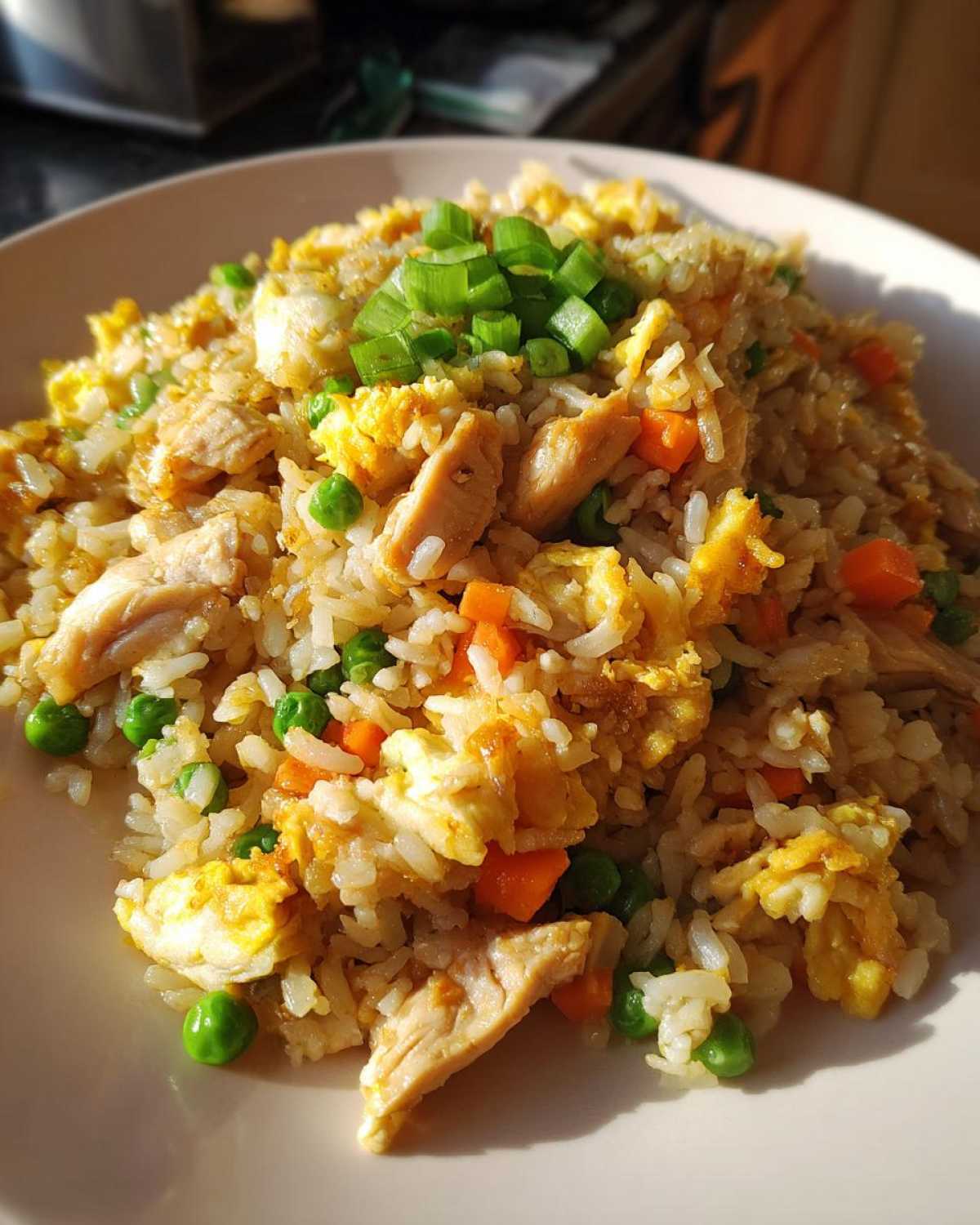 A close-up of a generous serving of homemade chicken fried rice, featuring visible pieces of chicken, egg, peas, carrots, and topped with green onions.