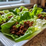 Close-up of several fresh chicken lettuce wraps filled with savory brown meat mixture and topped with green onions.