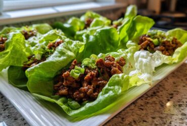 Close-up of several fresh chicken lettuce wraps filled with savory brown meat mixture and topped with green onions.