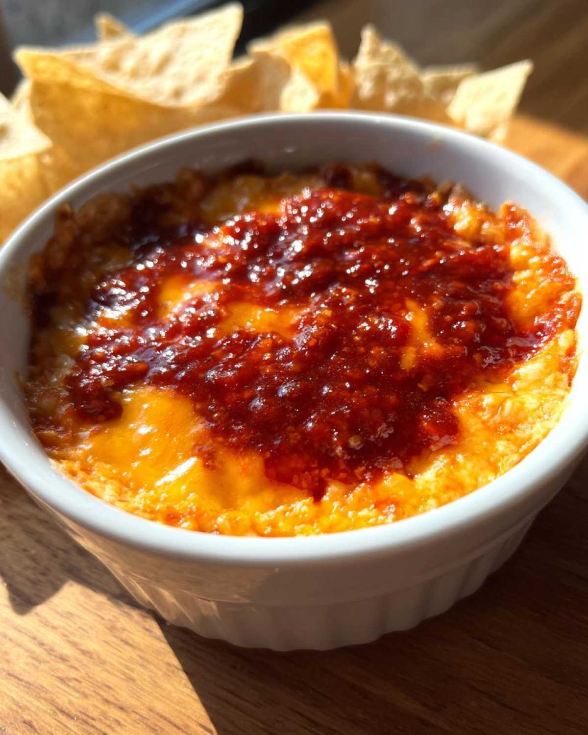 Close-up of hot chili cheese dip bubbling with melted cheese and chili topping in a white ramekin, served with tortilla chips.
