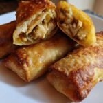 Close-up of four crispy, golden brown egg roll appetizers, one cut open revealing chicken filling.