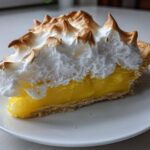 A close-up of a slice of amazing lemon meringue pie showing bright yellow filling and tall, toasted meringue peaks.