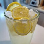 Close-up of a tall, sweating glass filled with homemade lemonade, ice cubes, and fresh lemon slices.