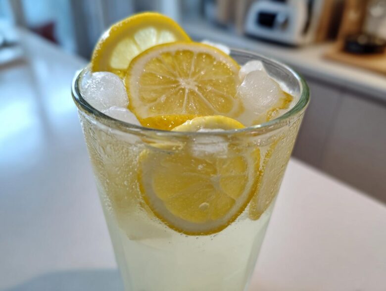Close-up of a tall, sweating glass filled with homemade lemonade, ice cubes, and fresh lemon slices.