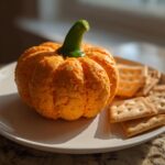 An amazing pumpkin cheese ball shaped like a small pumpkin, served with crackers on a white plate.