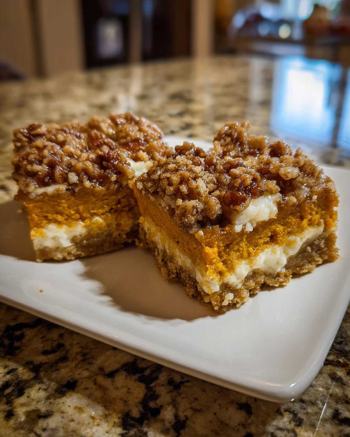 Two squares of layered pumpkin crunch dessert with a creamy layer and pecan topping on a white plate.