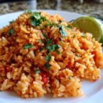 A mound of vibrant orange Spanish rice garnished with fresh cilantro and a lime wedge on a white plate.