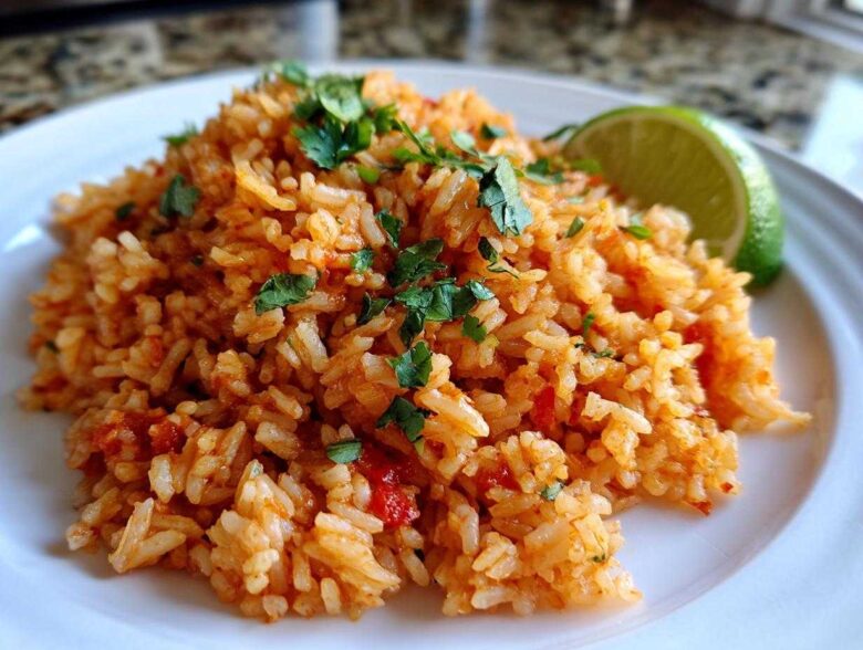 A mound of vibrant orange Spanish rice garnished with fresh cilantro and a lime wedge on a white plate.