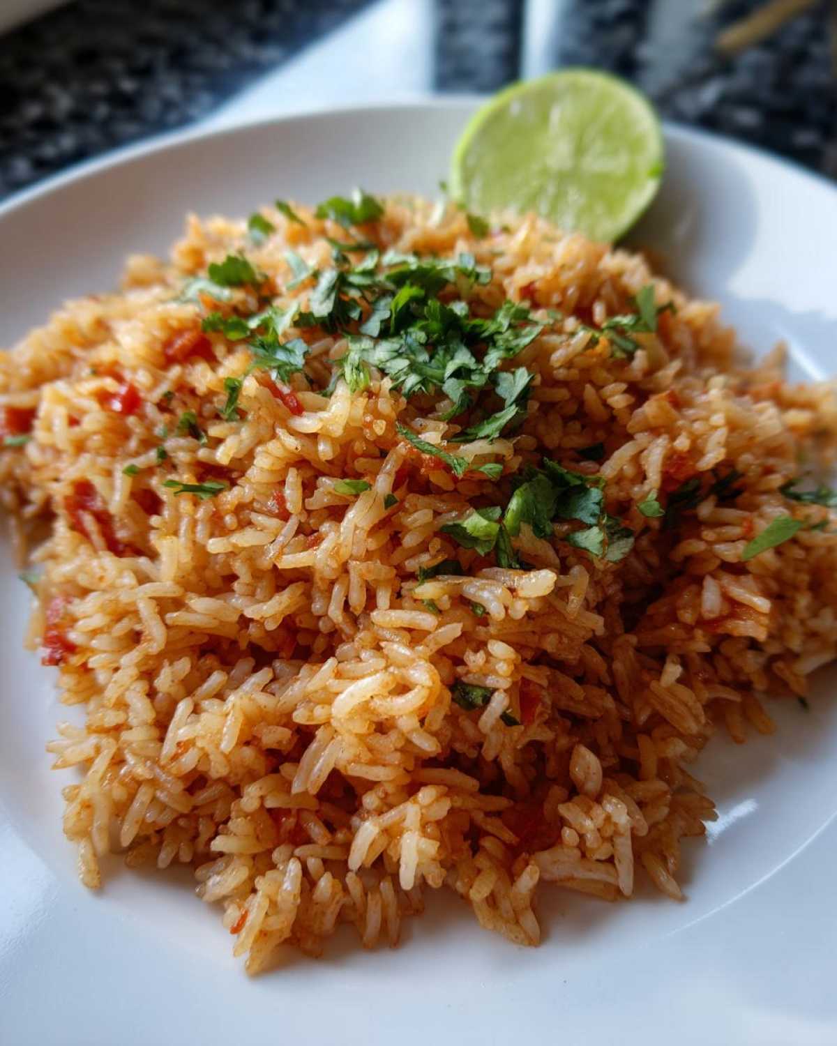 A close-up of perfectly cooked Spanish rice, garnished with fresh cilantro and a lime wedge.