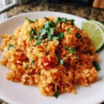 A close-up of a mound of fluffy, seasoned spanish rice topped with fresh cilantro and lime wedges.