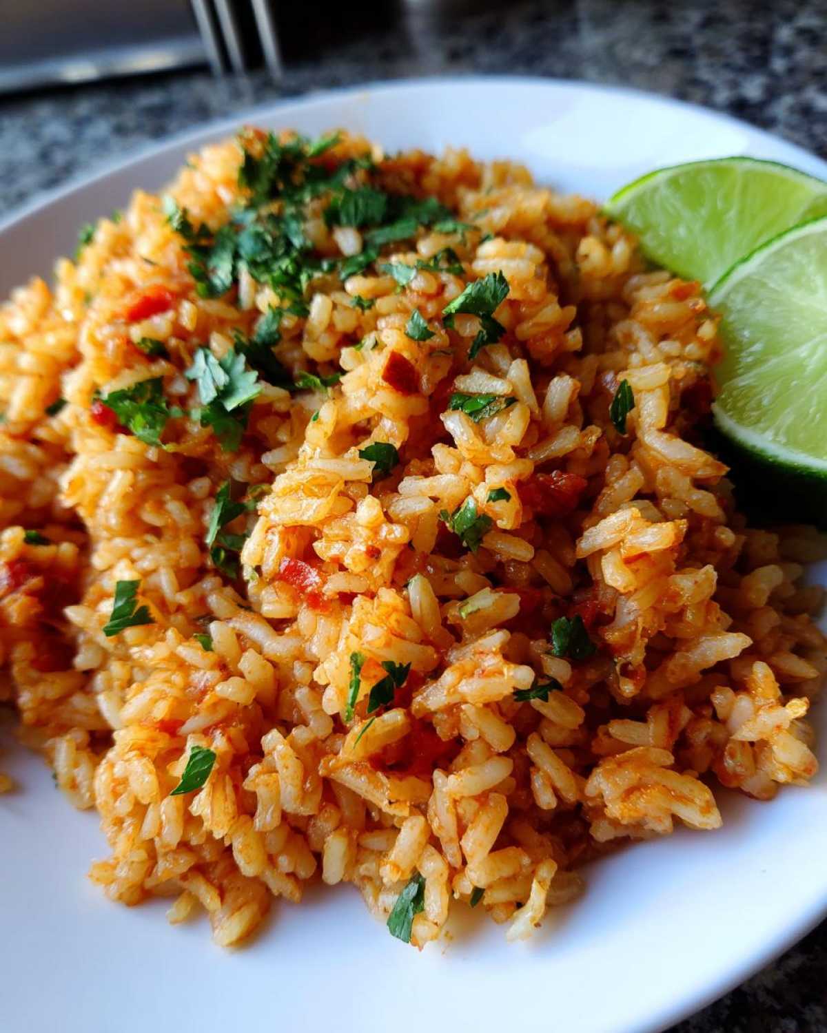 Close-up of a serving of vibrant orange Spanish rice topped with fresh cilantro and two lime wedges on the side.