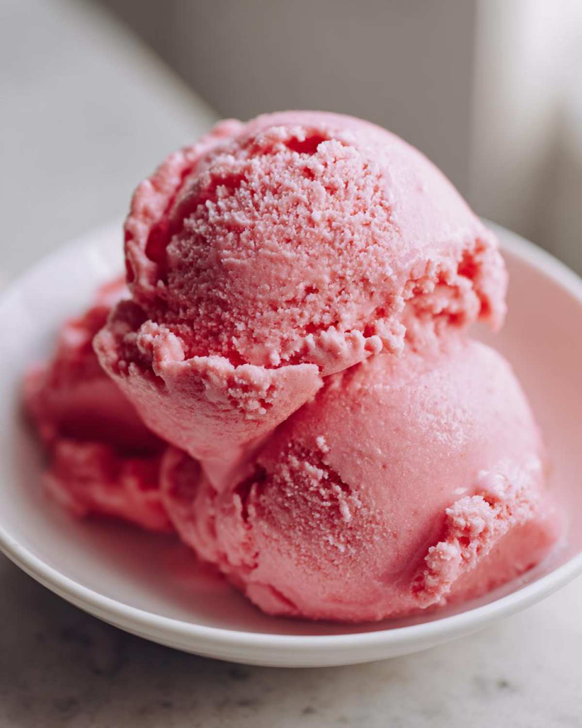Close-up of three scoops of bright pink strawberry ice cream in a white bowl.