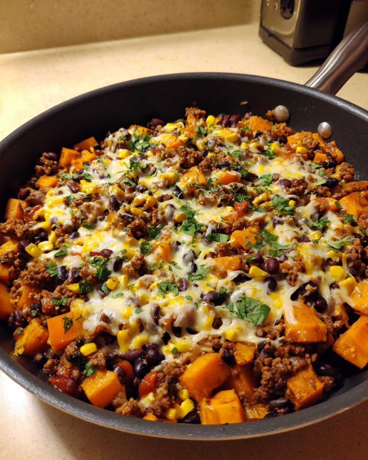 Close-up of a skillet filled with a savory sweet potato skillet dinner featuring ground meat, black beans, corn, melted cheese, and parsley.