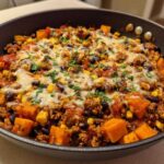 Close-up of a savory sweet potato skillet dinner with ground meat, black beans, corn, and melted cheese topping.