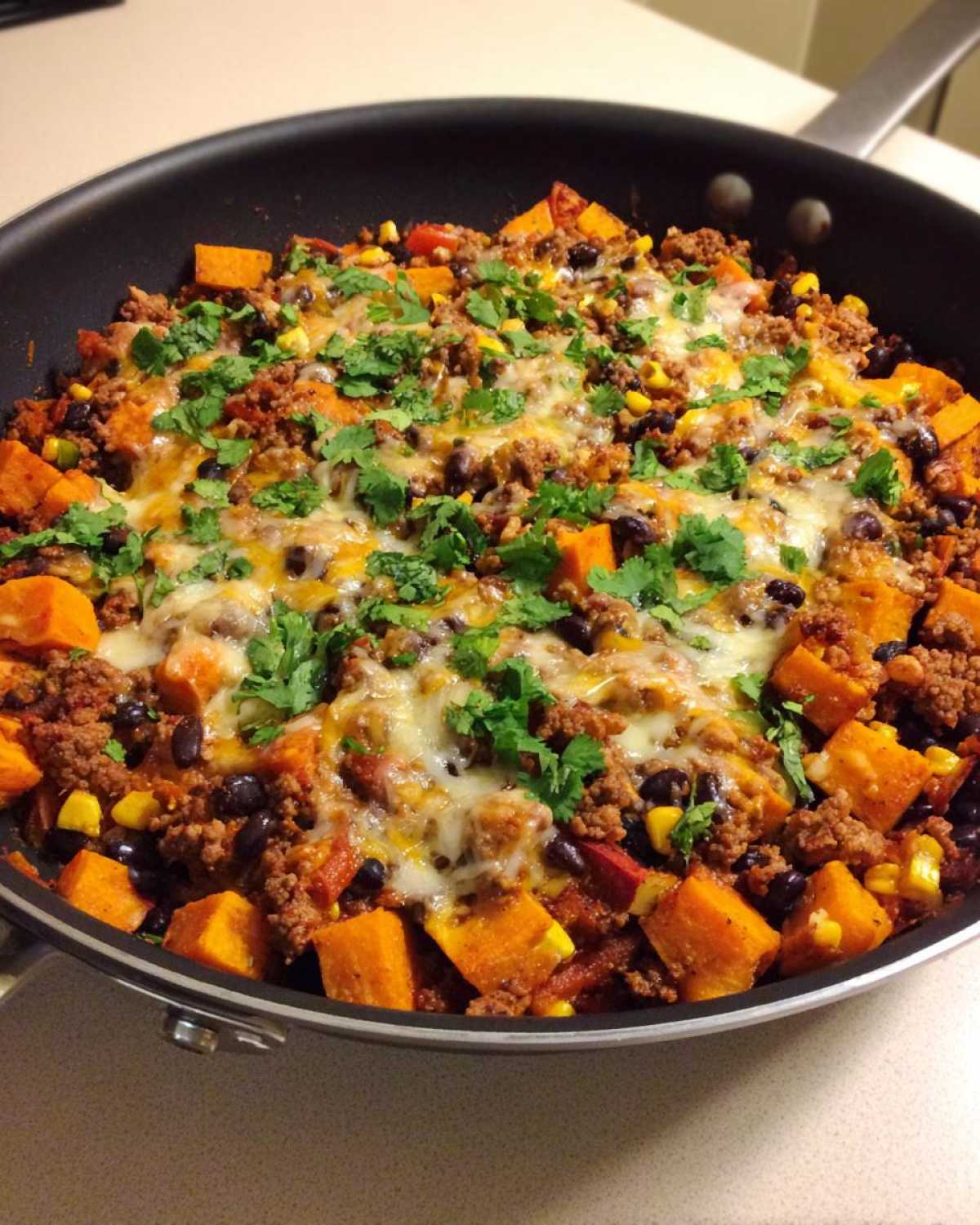 Close-up of an amazing sweet potato skillet with ground meat, black beans, corn, melted cheese, and fresh cilantro.