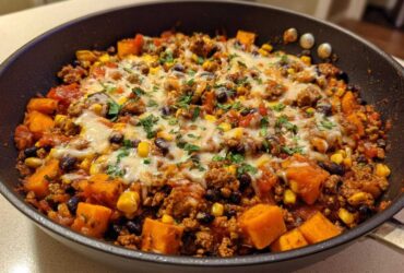 Close-up of a savory sweet potato skillet dinner with ground meat, black beans, corn, and melted cheese topping.