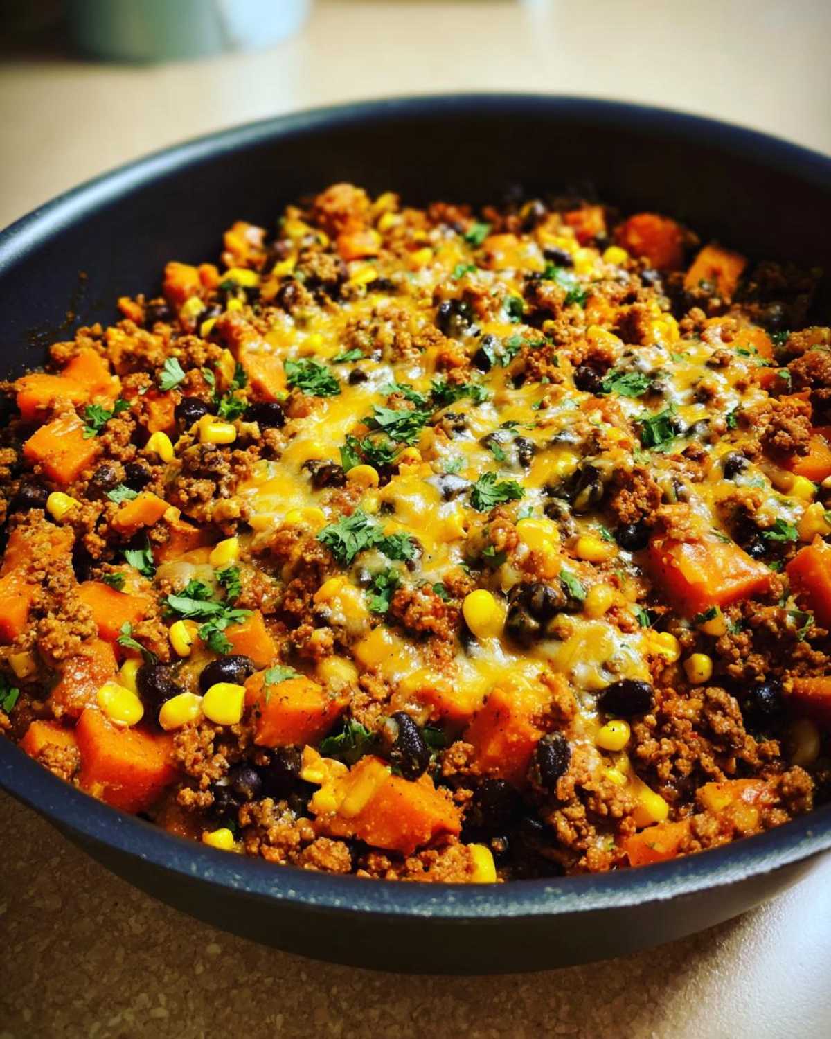 Close-up of a savory sweet potato skillet dinner featuring ground meat, black beans, corn, melted cheese, and cilantro.