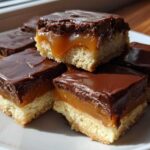 Close-up of several homemade twix bites featuring a shortbread base, gooey caramel, and thick chocolate topping.